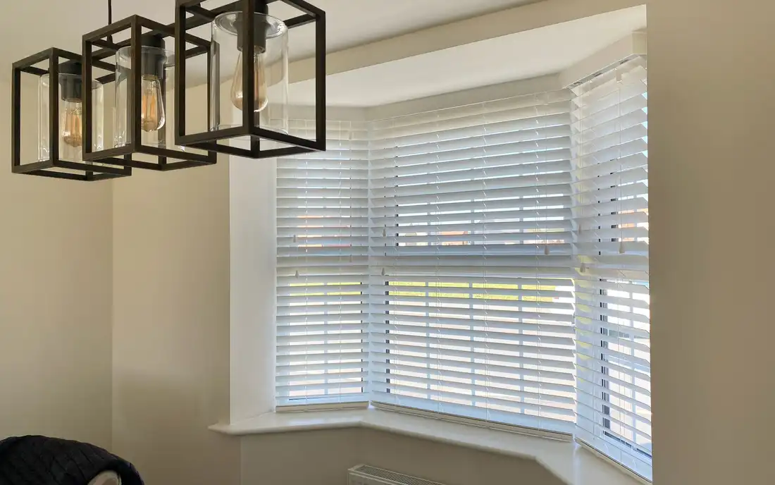 White wooden venetian blinds fitted across a bay window
