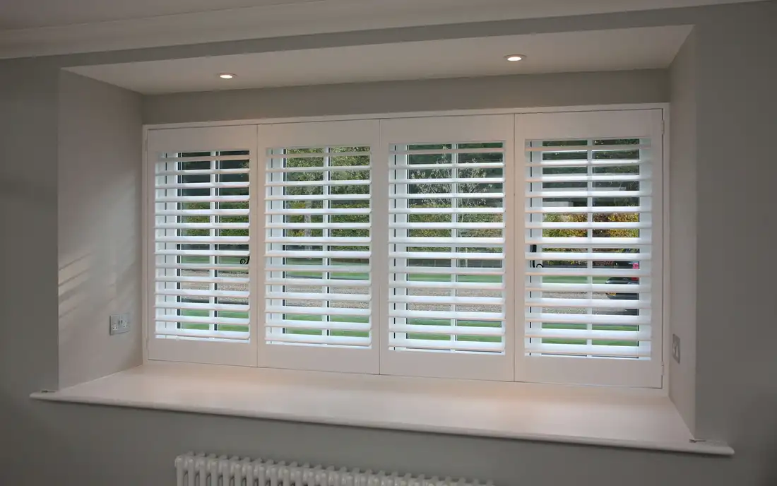 Made-to-measure white plantation shutters in a box bay window overlooking the garden