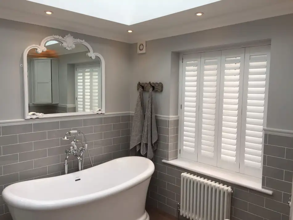 Waterproof shutters beside a freestanding bath in a grey-tiled bathroom