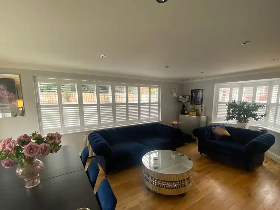 Wall-to-wall white shutters in a large Essex living room with navy sofas