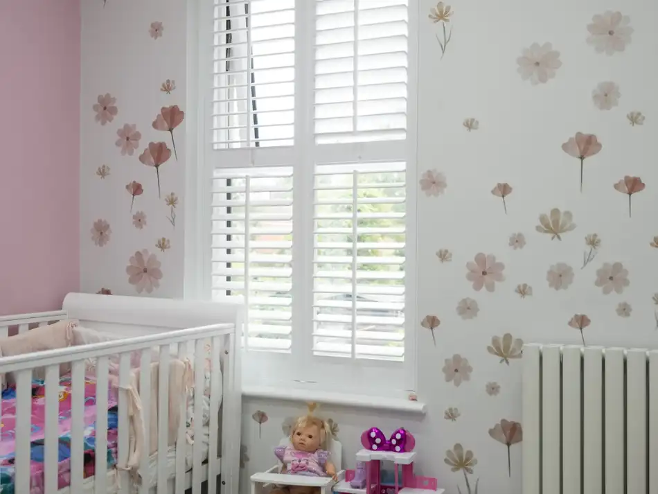 White shutters in a nursery with flower wallpaper and a cot